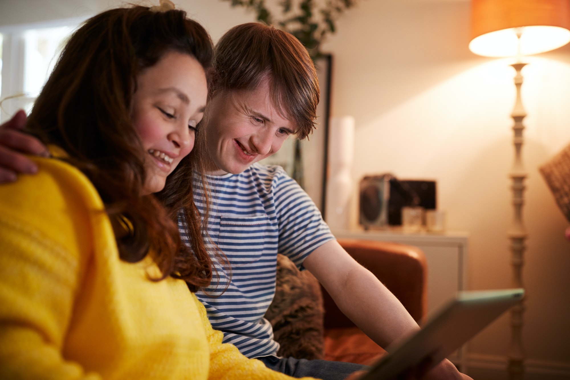 Young Downs Syndrome Couple Sitting On Sofa Using Digital Tablet At Home